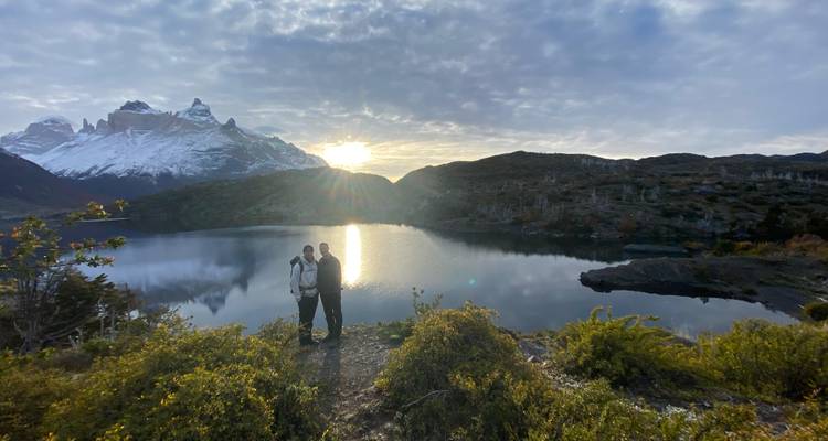 Dos excursionistas junto a un lago con fondo montañoso.