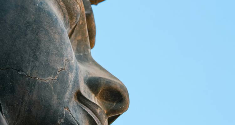 Gros plan de profil d'une statue antique contre un ciel bleu.