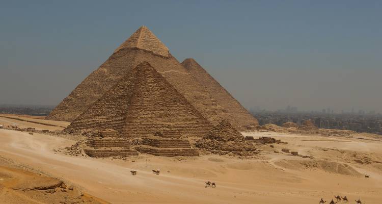 Pyramides de Gizeh avec un premier plan sablonneux et un horizon urbain.