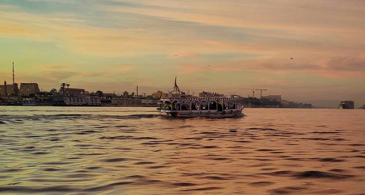 Bateau traditionnel sur une rivière au coucher du soleil près d'un paysage urbain.