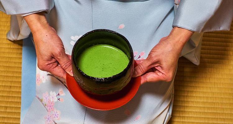 Gros plan de mains tenant un bol de thé matcha.