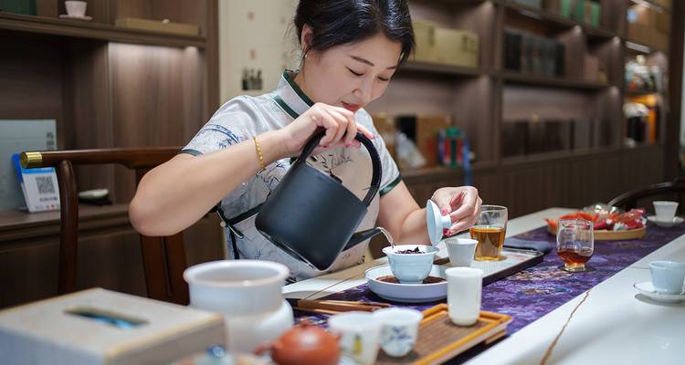 Une femme versant du thé dans un salon de thé traditionnel avec diverses tasses et théières.