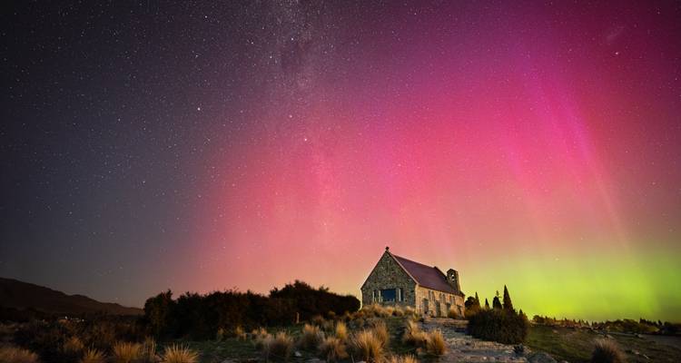 Kleine Steinkirche unter lebendiger Aurora in bergiger Gegend.