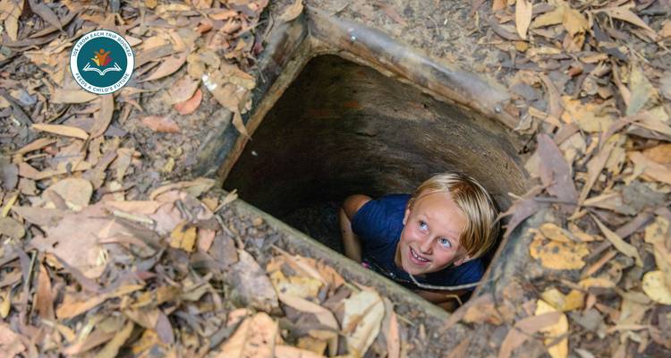 Enfant explorant l'ouverture d'un tunnel entouré de feuilles sèches.