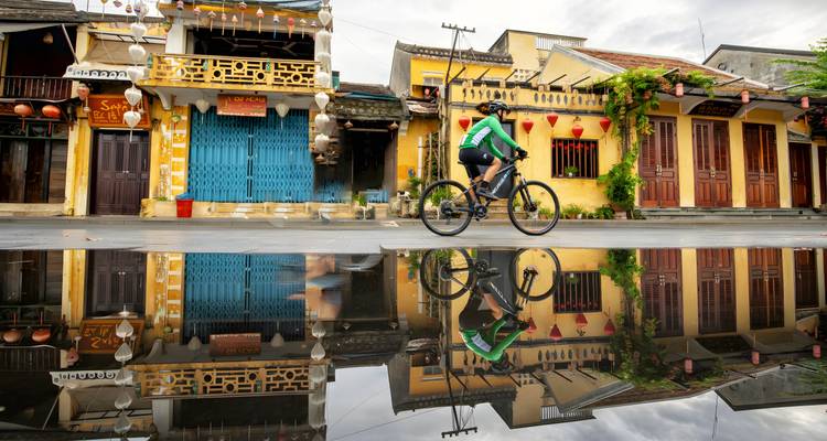 Cycliste reflété dans l'eau avec des bâtiments colorés en arrière-plan.