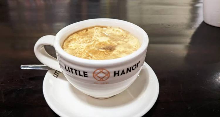 A cup with 'Little Hanoi' written on it, filled with coffee.