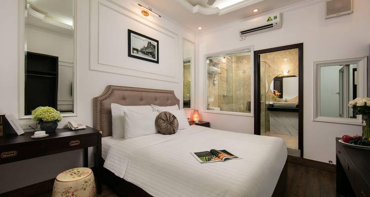 Cozy boutique hotel room in Hanoi with tufted headboard, modern bathroom and magazine on the bed.