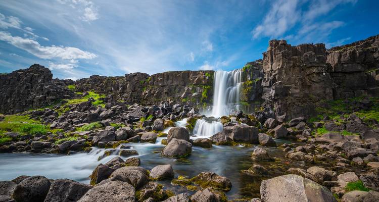 Waterfall amidst rocky landscape under a bright sky.