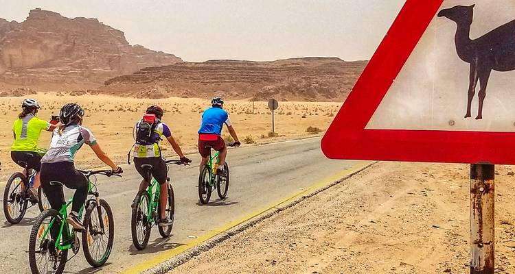Cyclistes passant devant un panneau de chameau dans le désert, Wadi Rum, Jordanie.