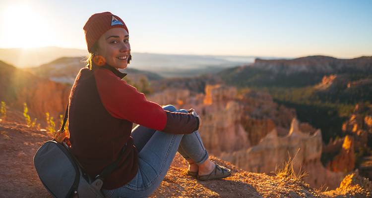 Femme assise au bord d'une falaise à Bryce Canyon au coucher du soleil.