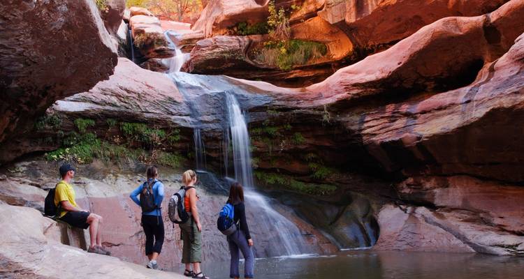 Un groupe de randonneurs debout près d'une petite cascade entourée de roches rouges.