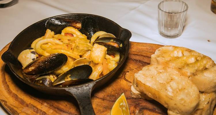Poêle avec plat de fruits de mer et pain sur une planche de service en bois.