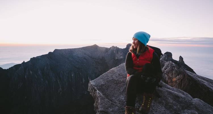 Personne assise sur un rocher avec vue sur la montagne au lever du soleil.