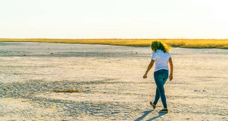 Woman walking across a vast, dry landscape.