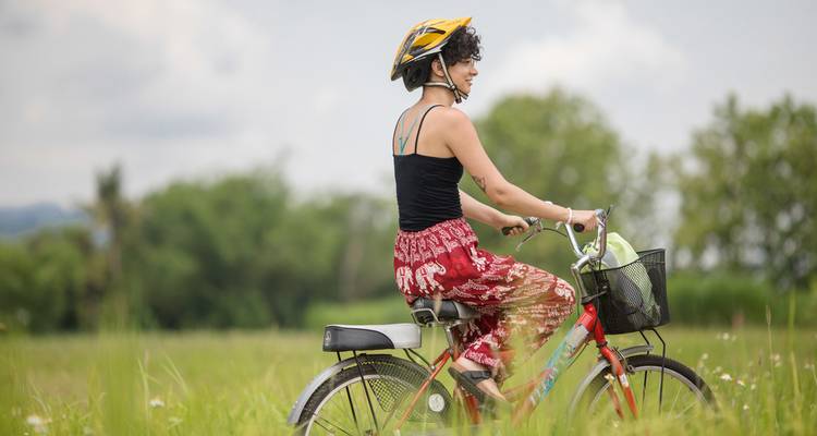 A woman cycling in a green field with bushes in the background.