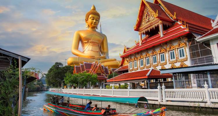 Golden Buddha statue next to a red temple by a canal.