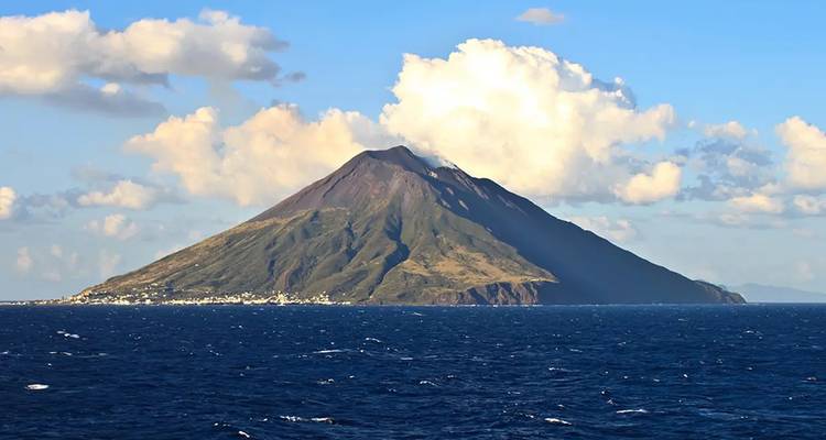 Le volcan conique du Stromboli s'élève dramatiquement de la mer Tyrrhénienne bleue sous des nuages bouffants.
