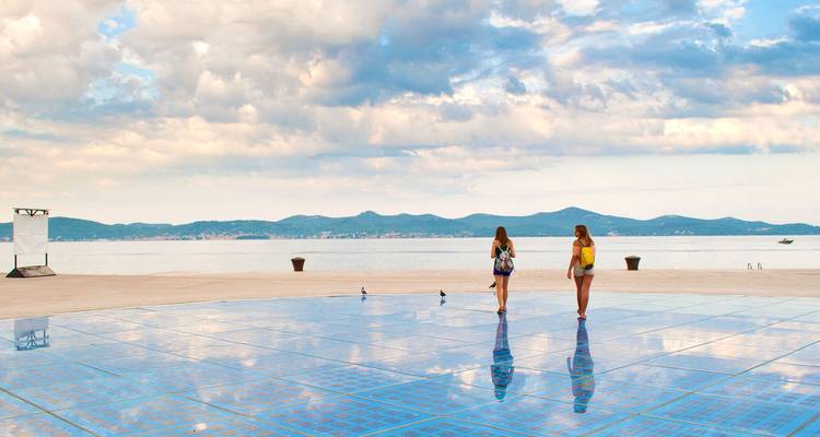 Deux personnes marchant sur une place éclairée au bord de la mer.