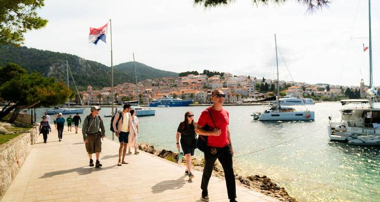 Des gens marchant le long d'une côte avec des yachts et une ville en vue.