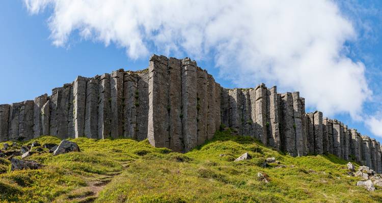 Hexagonal basalt columns on a grassy hill under a clear sky.