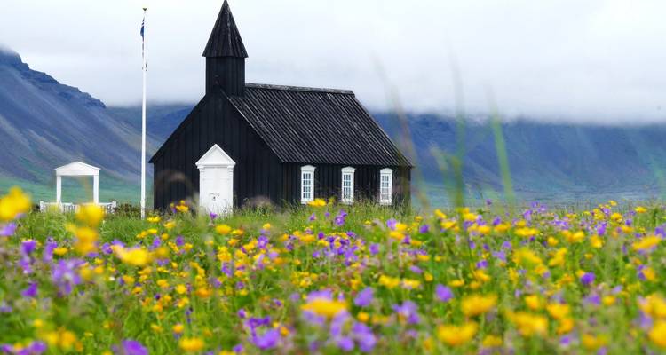 Black church surrounded by colorful wildflowers with mountains in the background.