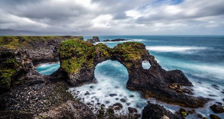 Rock formation arch with waves crashing in a dramatic seascape.