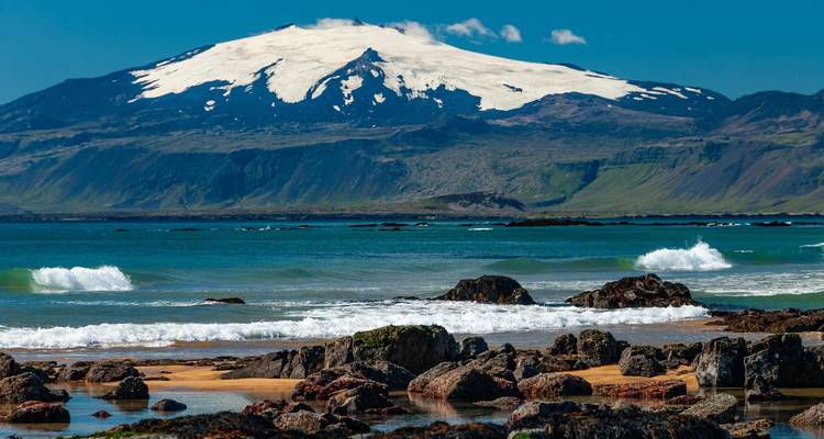 Snow-capped mountain overlooking a rocky coastline and ocean.