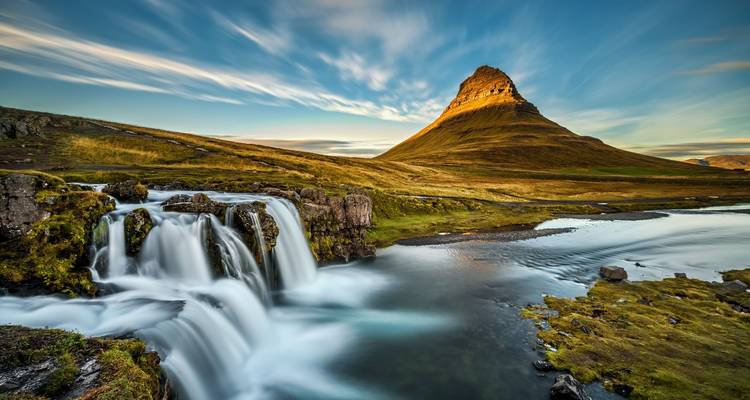 Waterfall and river with Kirkjufell mountain in the background at sunset.