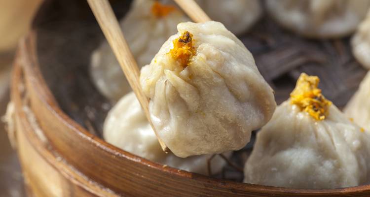 Close-up of Chinese dumplings held with chopsticks in a steamer.