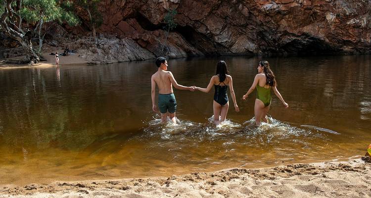 Drie mensen die een waterpoel inlopen omringd door rode rotsen.