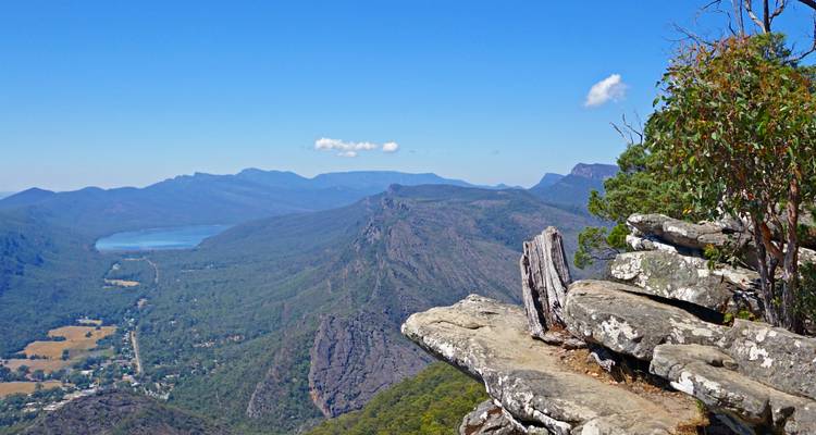 View from a rocky outcrop overlooking a wide expanse of mountains and a valley.