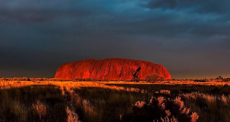 Uluru au coucher du soleil avec des teintes rouges vibrantes et des ciels dramatiques.