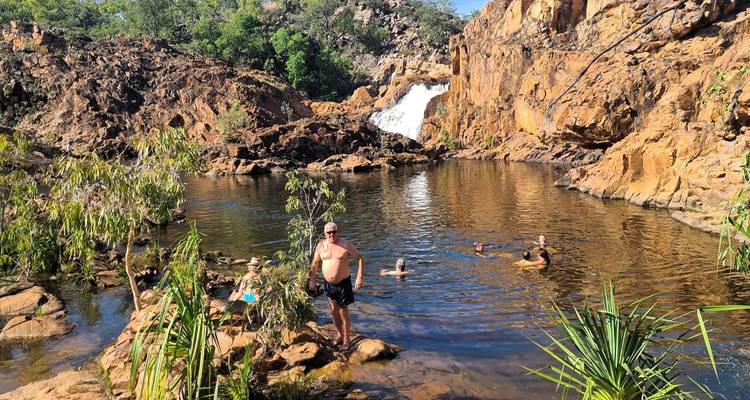 Groupe de personnes nageant dans un bassin naturel avec une cascade.