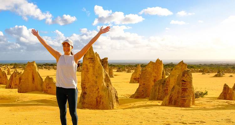 Viajero con los brazos levantados de alegría en medio de las agujas de piedra caliza amarilla del Desierto de los Pináculos.