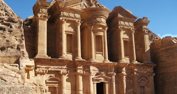 La fachada monumental de arenisca del Monasterio de Petra se alza bañada por la luz del sol contra un cielo azul despejado.