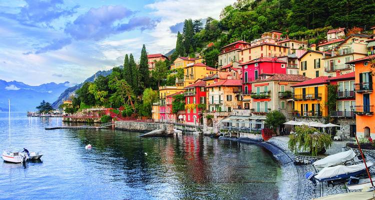 Maisons colorées du village au bord du lac se reflétant dans les eaux calmes avec des pics alpins lointains