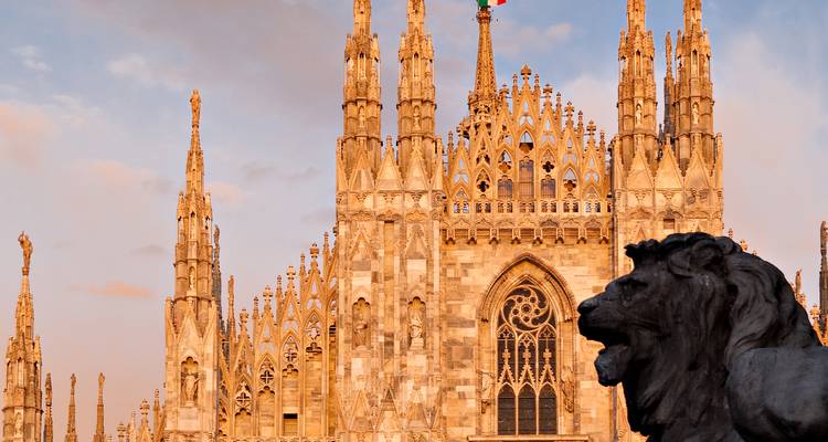 La cathédrale de Milan au coucher du soleil avec une statue de lion au premier plan.