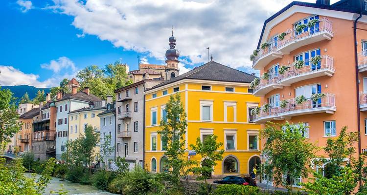 Casas a orillas del río pintadas de colores brillantes y campanario de la iglesia en la ciudad alpina de Merano.