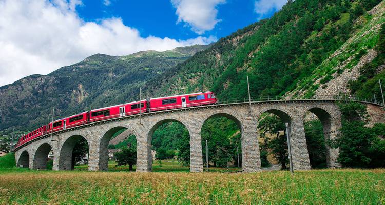 Red Bernina Express train curving over a stone viaduct in a lush alpine valley