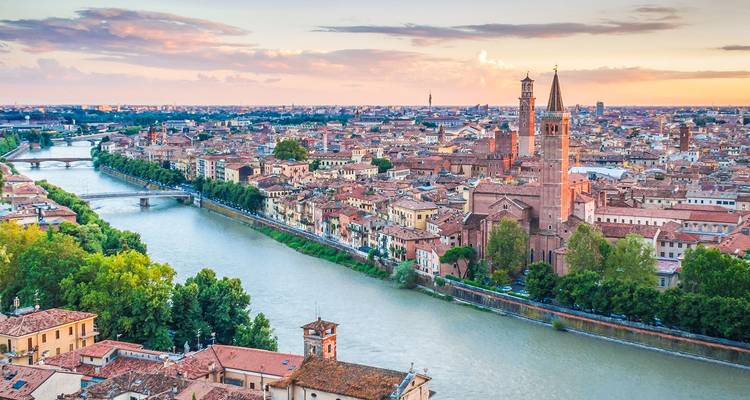 Golden-hour aerial of Verona’s skyline along the Adige River and tall church spires
