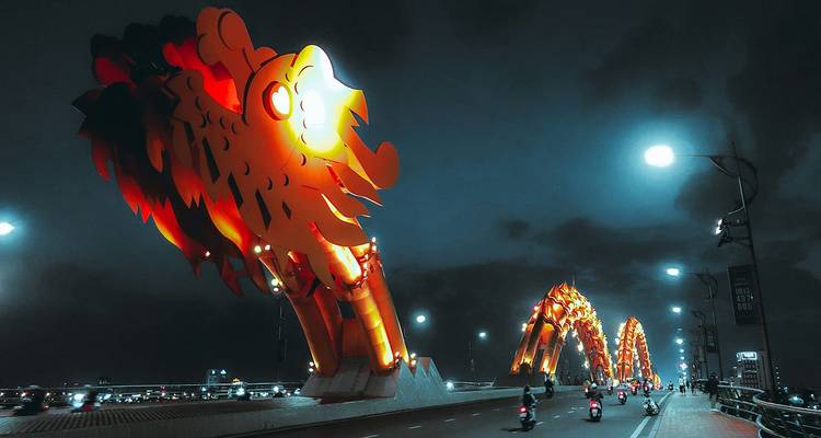 Le Pont du Dragon illuminé à Da Nang brillant en orange la nuit avec des motos traversant la travée.