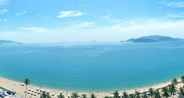 Vista panorámica del mar turquesa encontrándose con una larga playa de arena y islas lejanas.