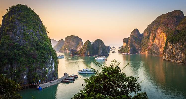 Boats in a bay surrounded by limestone karsts at sunset.