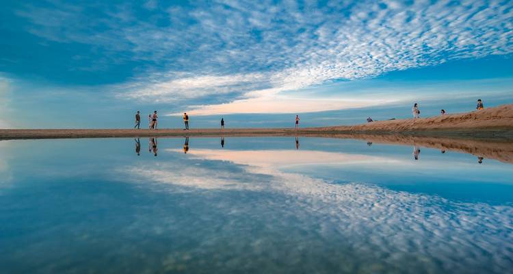 People walking on a beach with reflections in the water.