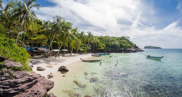 Beach with boats and people swimming in clear water.