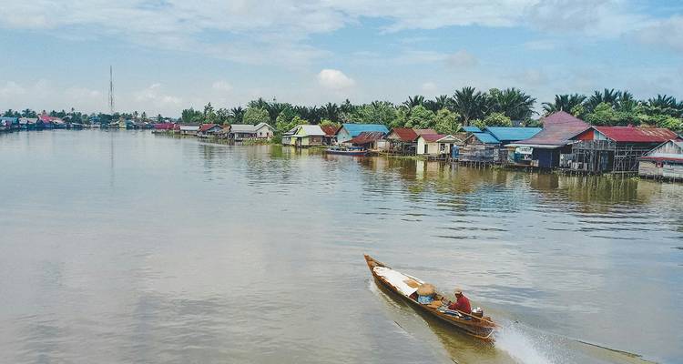 Stilt houses and boat on a river under partly cloudy sky.