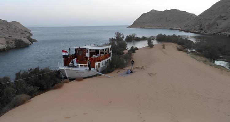 Boat docked by a sandy shore with desert scenery.
