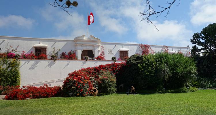 White colonial building with a flag and lush garden.