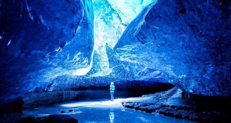 Person standing in a stunning blue ice cave.