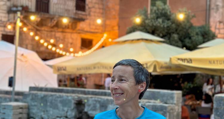Femme profitant d'une soirée dans un café en plein air avec des guirlandes lumineuses chaudes et des murs de pierre rustique derrière elle.